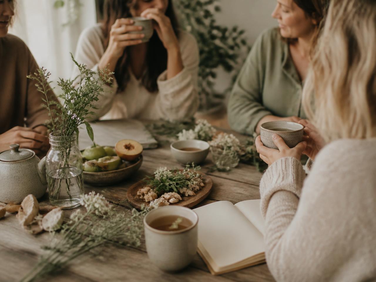 A small group gathered around a wooden table with herbal tea, whole foods, and an open notebook